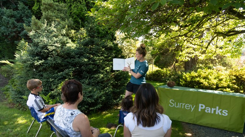 Staff reads a story book to a group of children and parents in the park