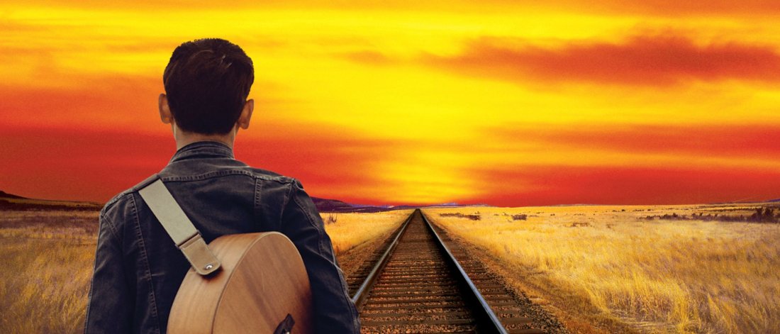 A man with a guitar over his shoulder looks into a glorious sunset