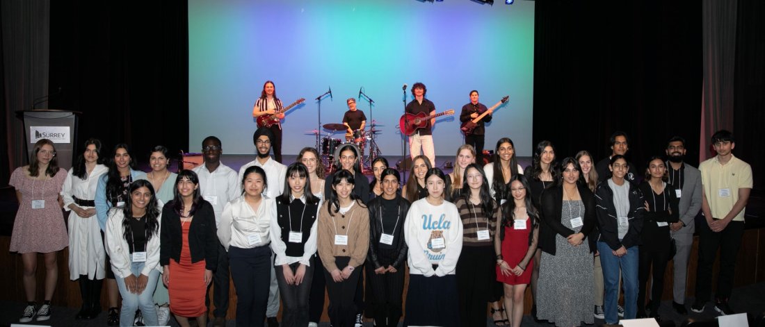 A group of young attendees and musicians on stage at a conference or awards event, posing together for a photo.