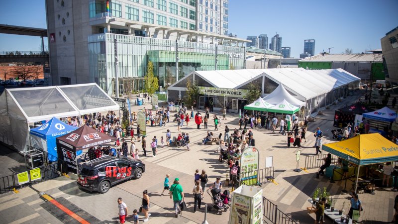  An outdoor event with tents, crowds, and city buildings in the background on a sunny day.