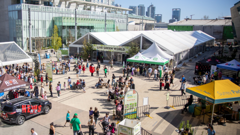 An outdoor event with tents, crowds, and city buildings in the background on a sunny day.
