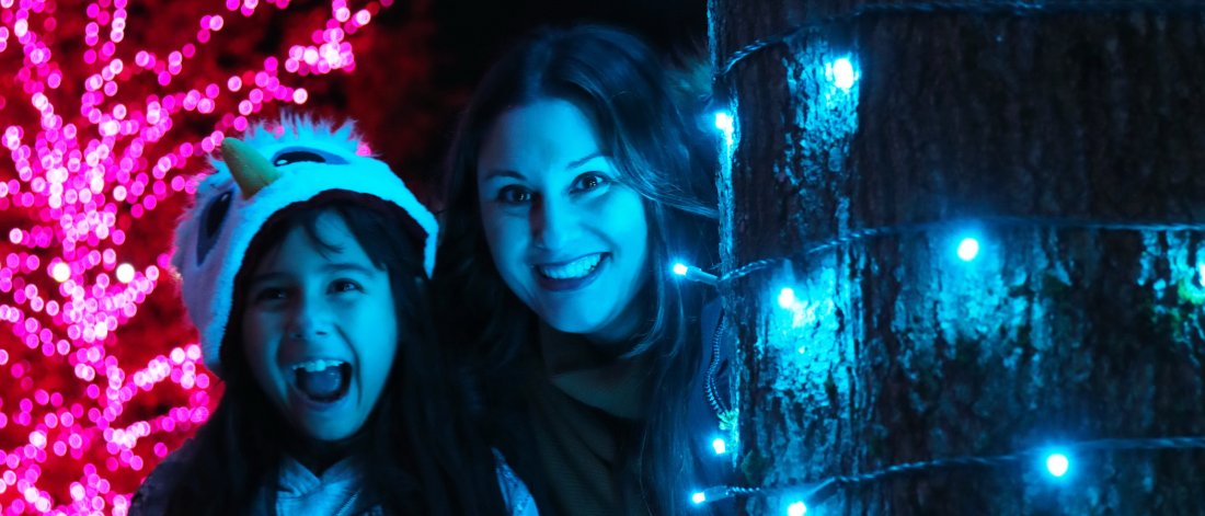 a mother and daughter beside some holiday lights
