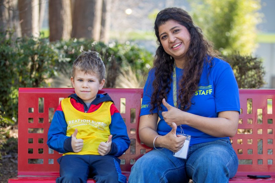 A child and adult sitting on a red bench outside.