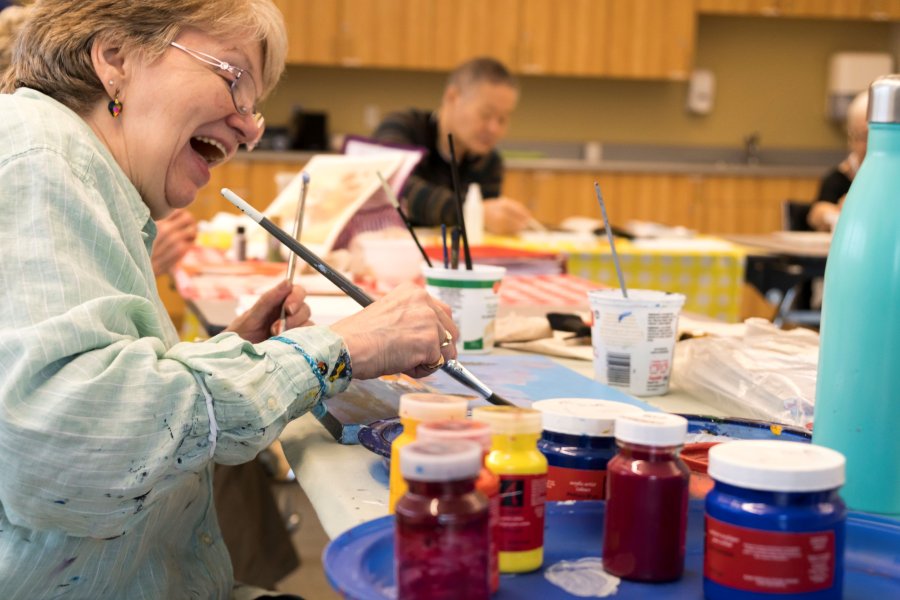 A senior woman painting and laughing.