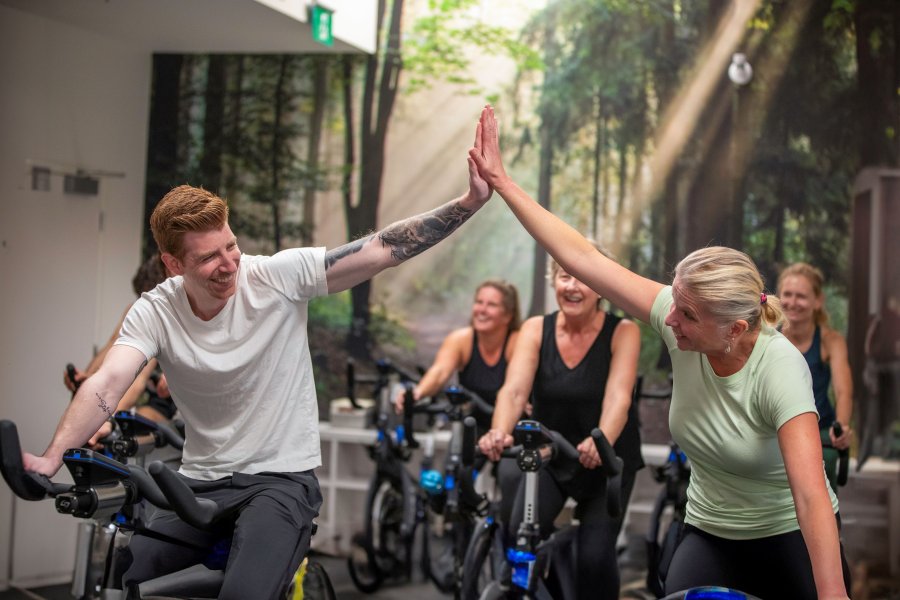Two people high-fiving as they're riding an indoor bike.