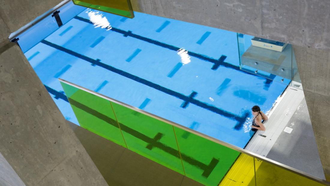A view of a pool from a diving board with one female swimmer