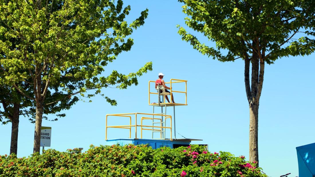 A man sits in a lifeguard station with trees on either side
