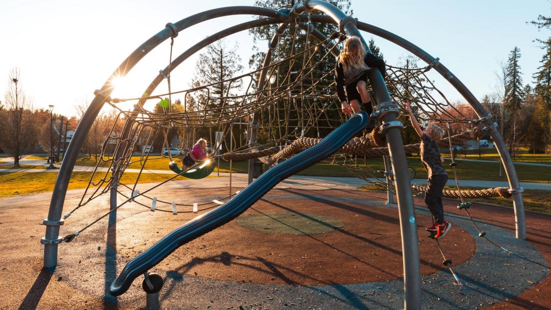 Two children on a rope climbing play structure at a park