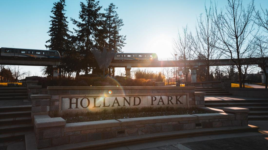 Holland Park concrete sign with a skytrain in the background
