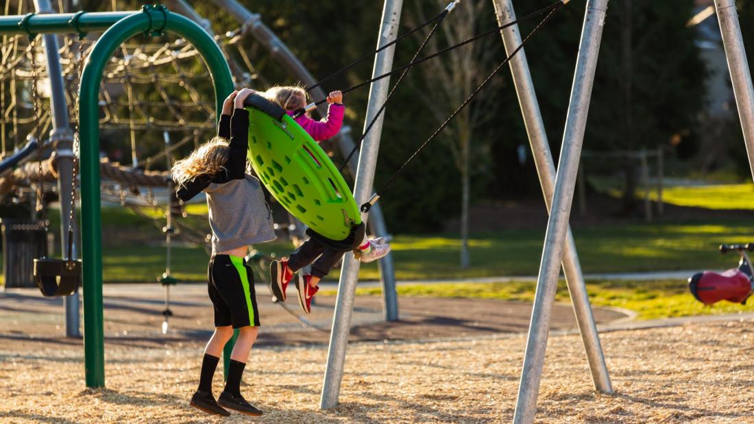 A child pushes another child on a green disc swing