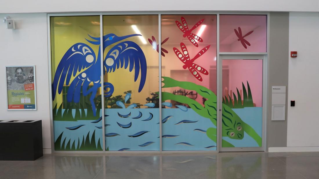 Colourful Indigenous art of dragonflies, a frog, and a heron on an indoor window