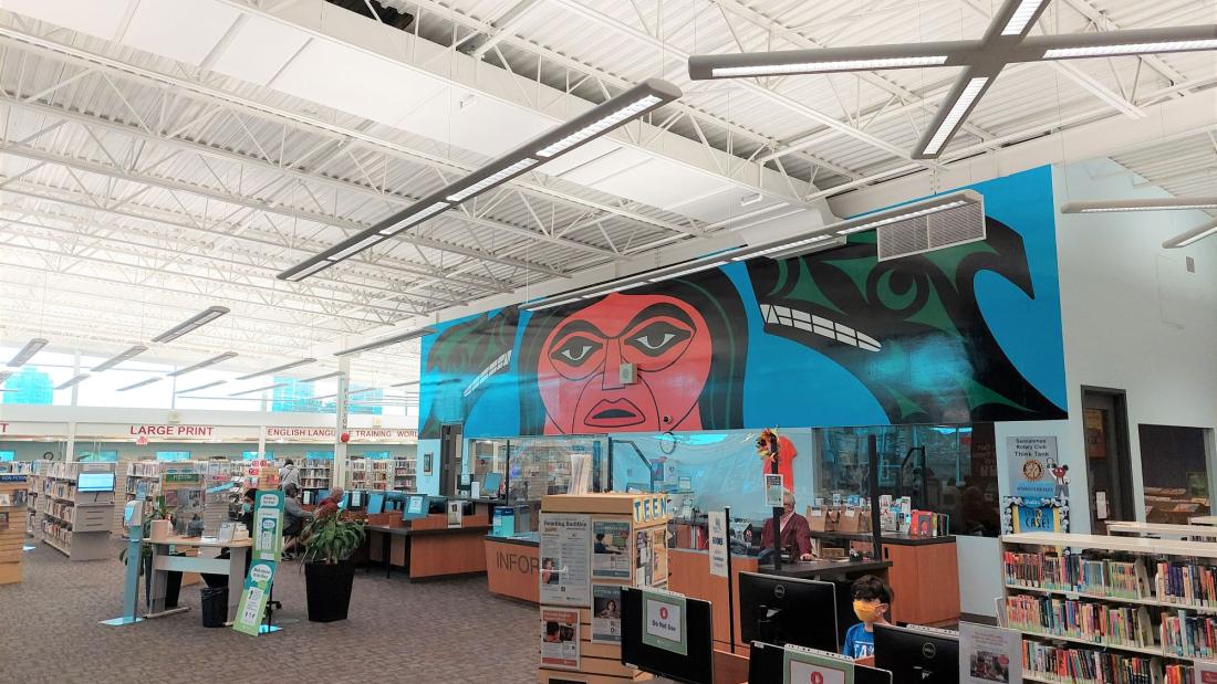 A mural above computers inside a library. An Indigenous man with two wolves