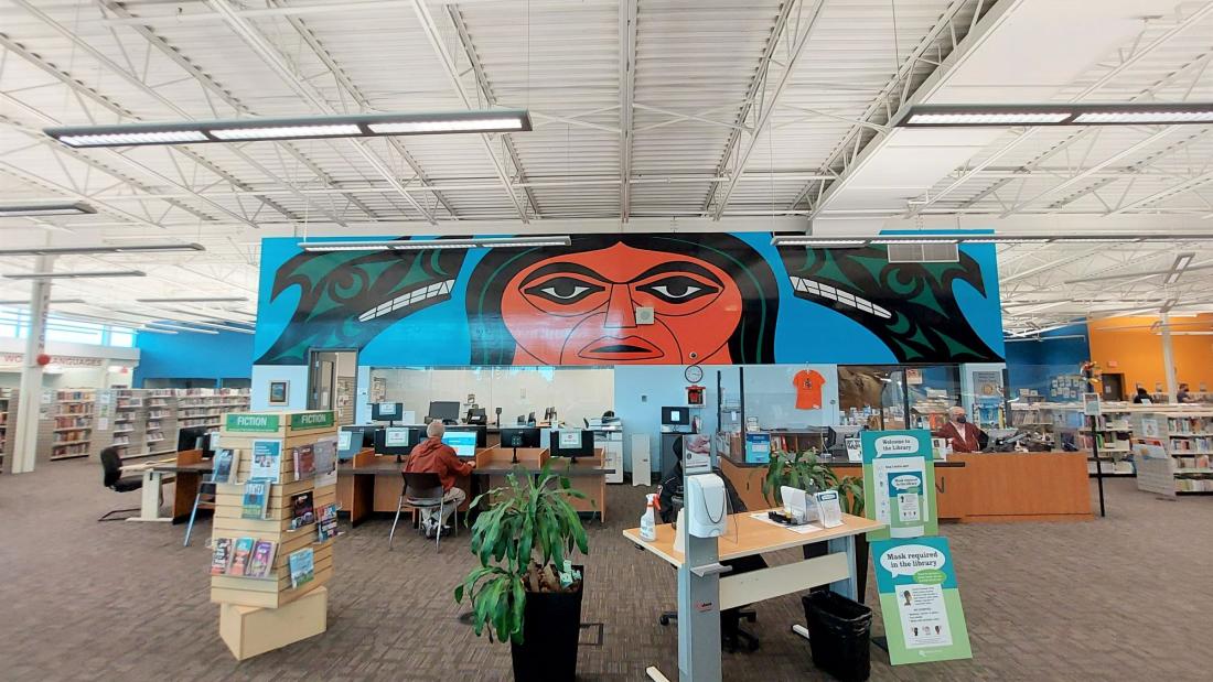 A mural above computers inside a library. An Indigenous man with two wolves