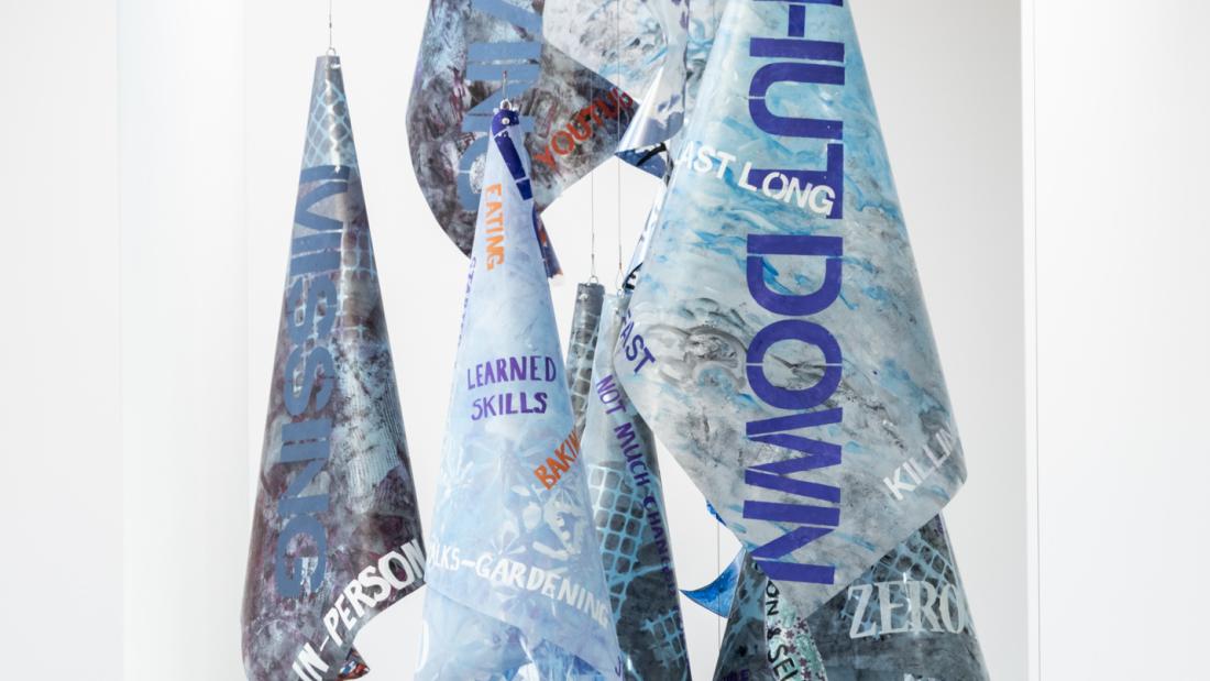 Image of a hanging sculpture made from acetate sheets rolled into cones and hung in spirals, painted in shades of blue with words stenciled on.