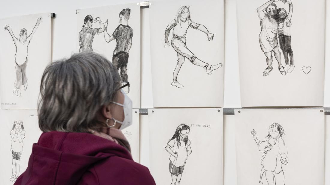  Image over the shoulder of a person in a red coat, looking at a wall of life drawings.