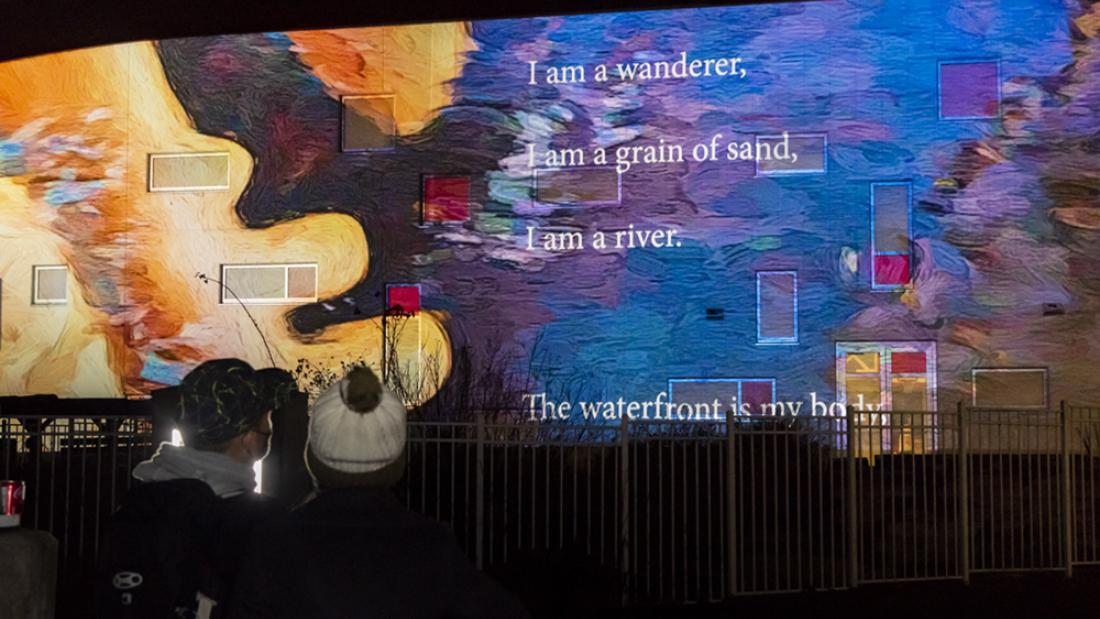 Installation view of Body as Border: Traces and Flows of Connection. Two figures stand in front of the artwork, which features poetry, bacterial samples, and digital painting.