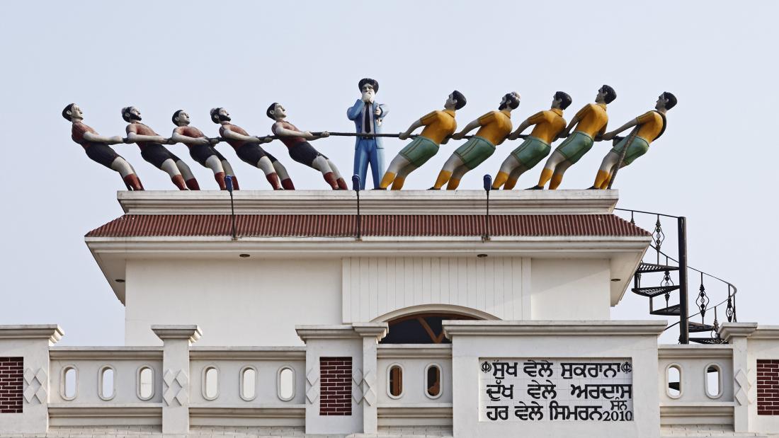 Photograph of a rooftop sculpture in India's Punjab showing 5 figures pulling on each side of a tug of rope.