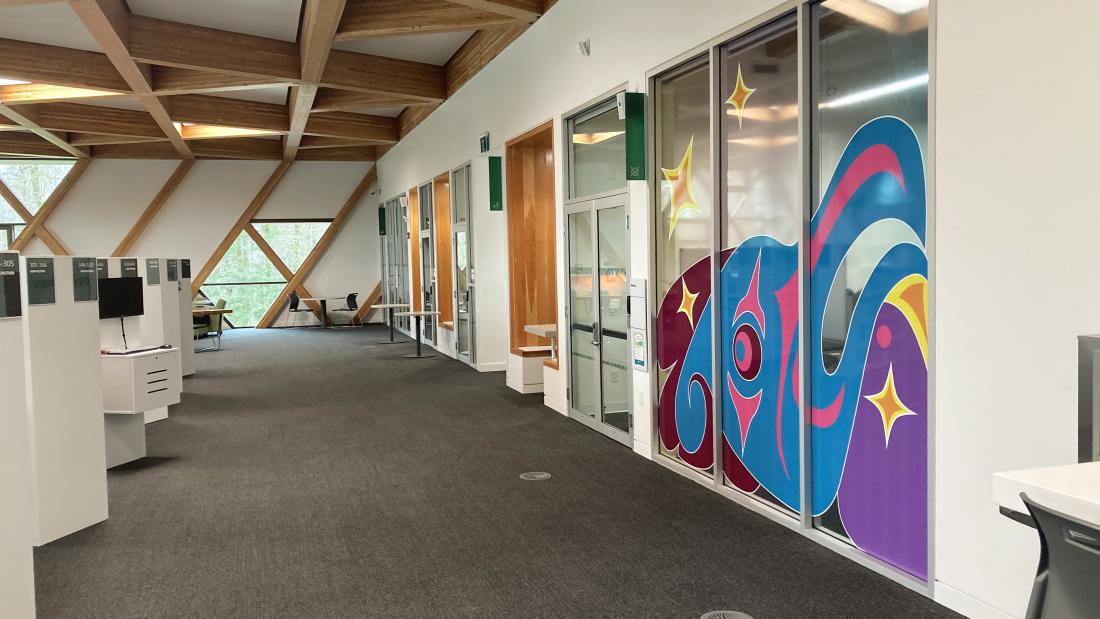 A colourful artwork on a 3-panel window of a meeting room off to the right of a library.