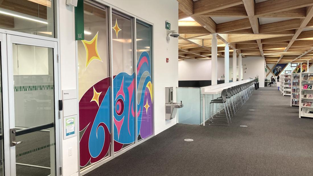 A colourful artwork on a 3-panel window of a meeting room off to the right of a library.