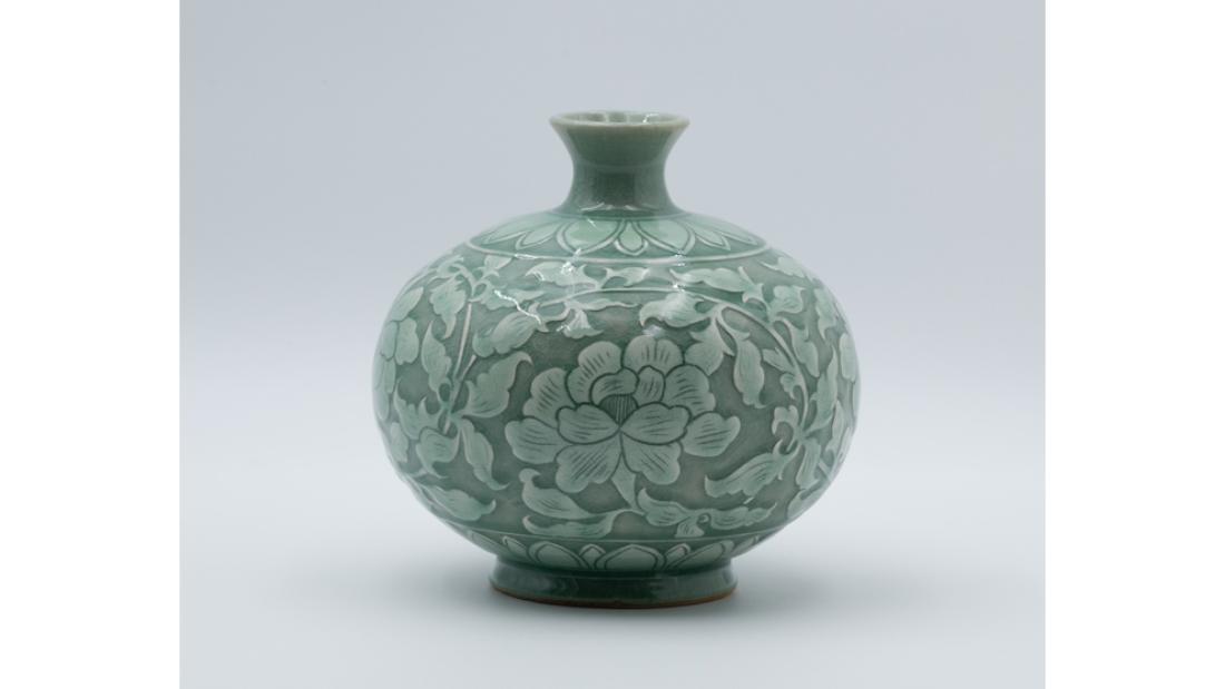 Green ceramic vase with wide body and thin neck, covered with peonies.