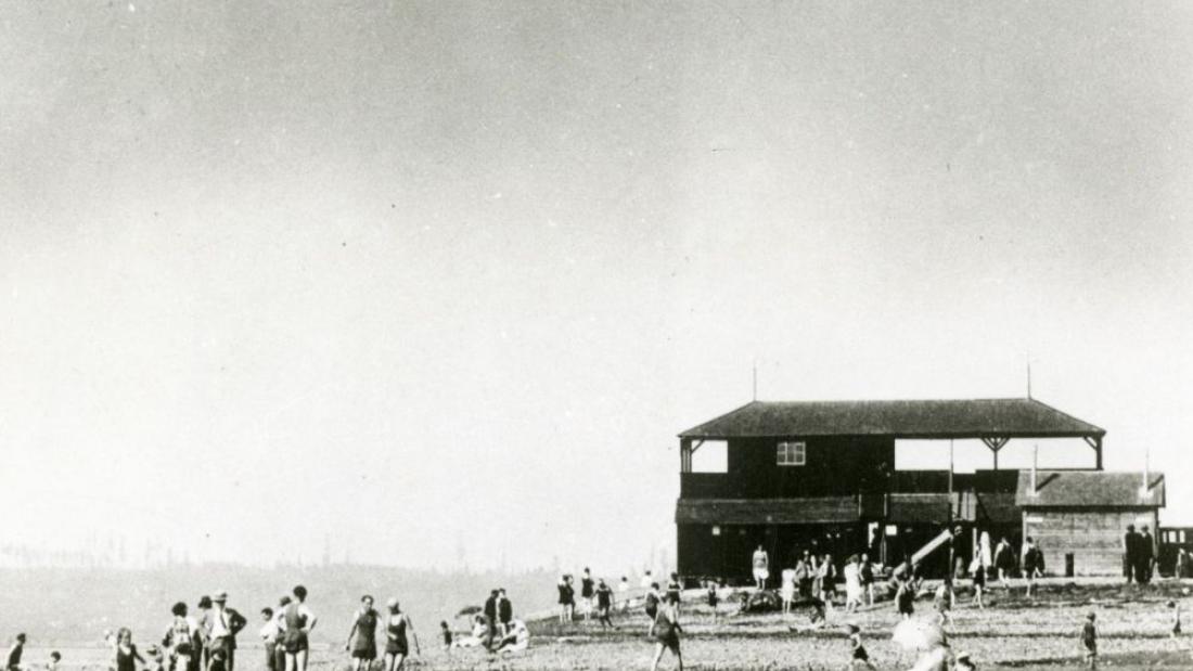 People at the beach with the boathouse in the background