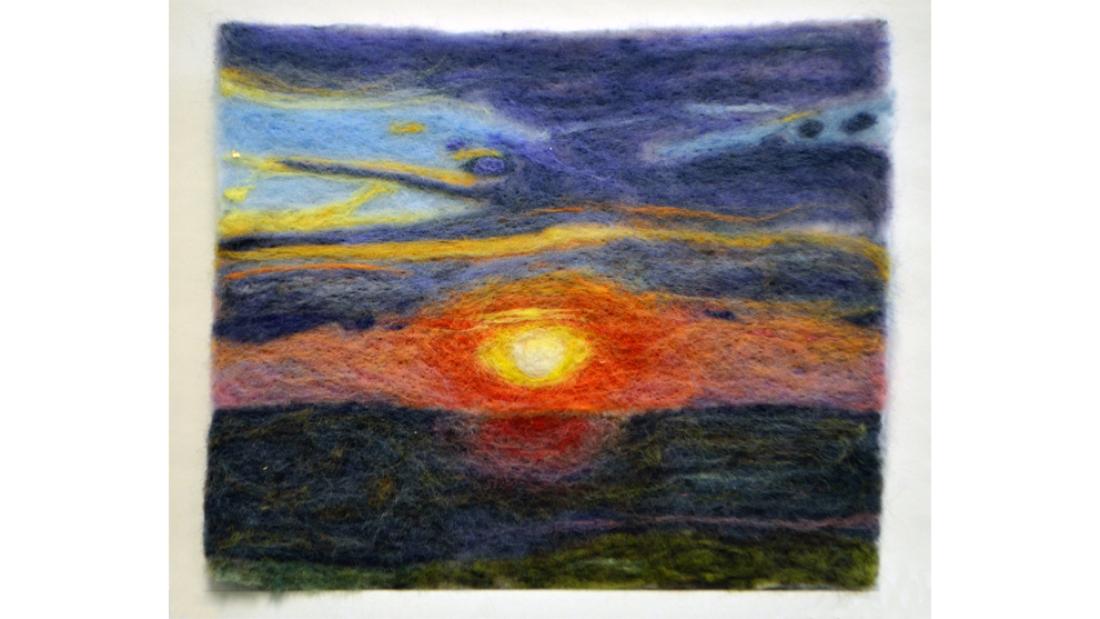 Colourful felt artwork of a setting sun against a dramatic blue sky.