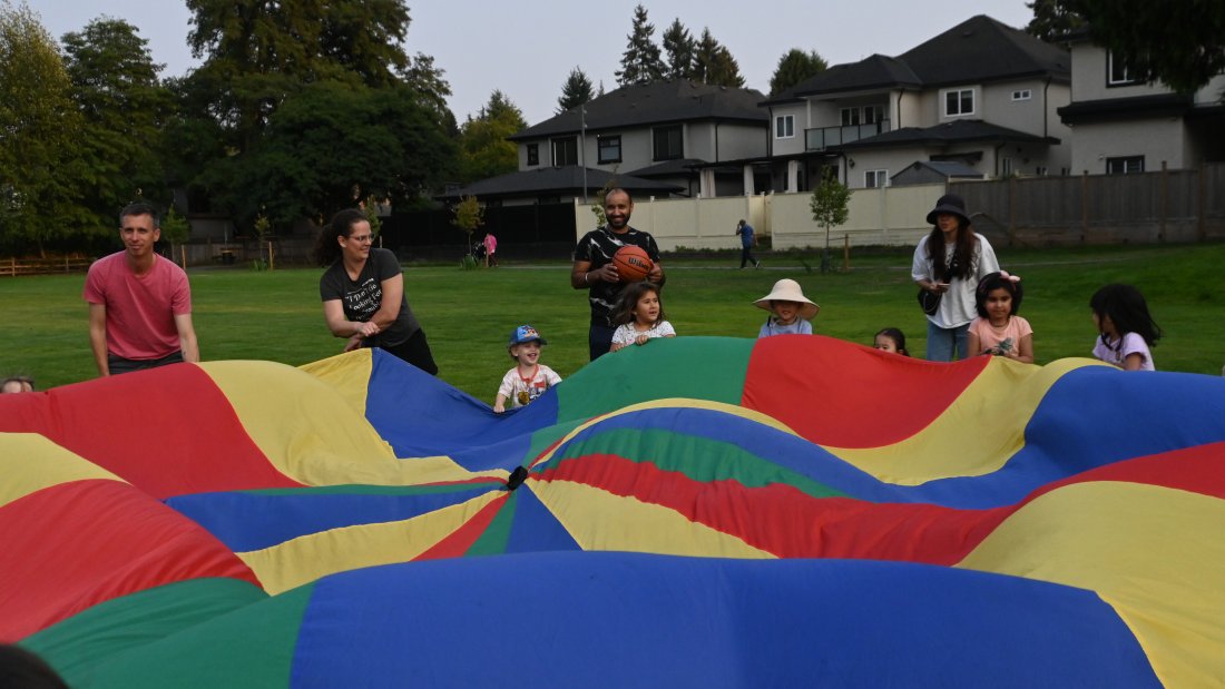 A group of children and adults play a parachute game