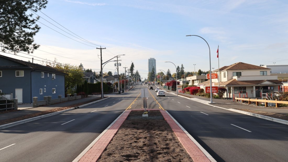 This image shows a well-maintained urban road viewed from the center, with a median strip covered in red bricks.