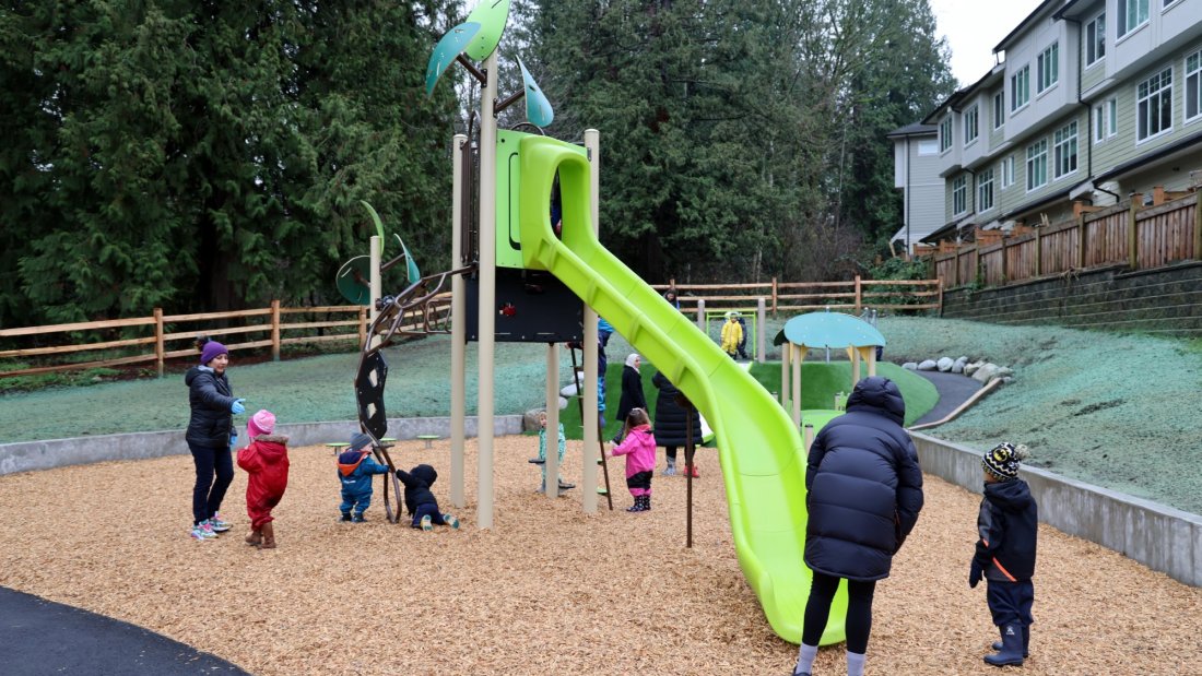 a park with large trees, a playground, and townhomes in the background