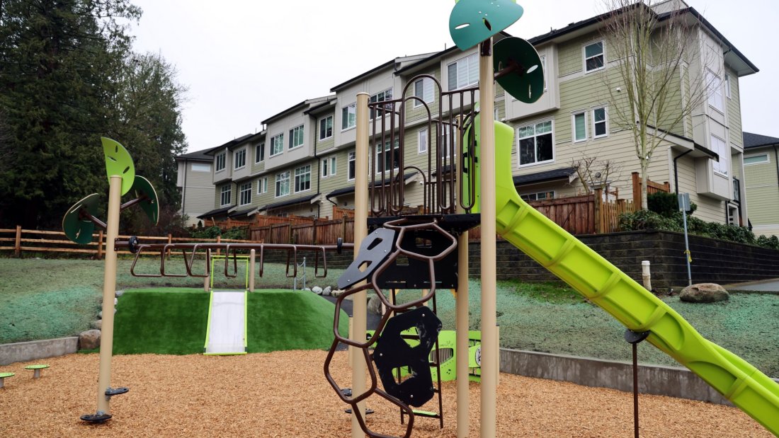 a park with large trees, a playground, and townhomes in the background
