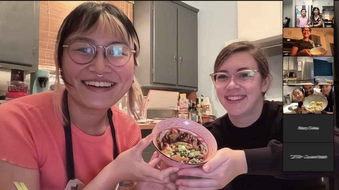 A Zoom screenshot of two people holding up a bowl of dumplings.