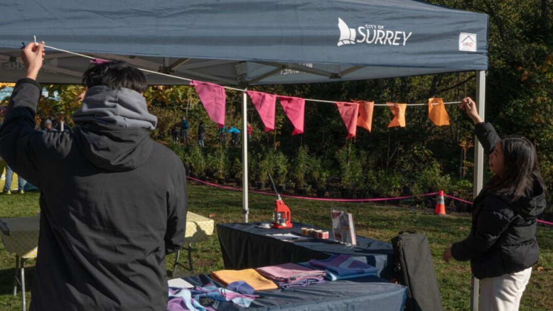 two people setting up fabric flags at a tent with the words "our city"