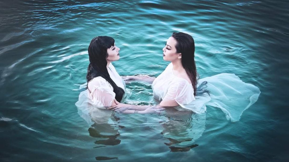 Two women in white dresses float in water, gazing at each other.