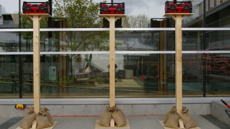Three red boom boxes on fence posts 