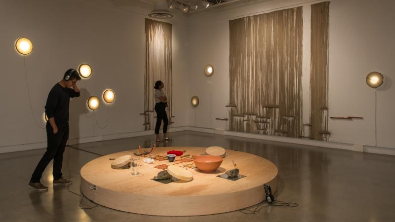 Art gallery visitors examine a circular stage with bowls on it