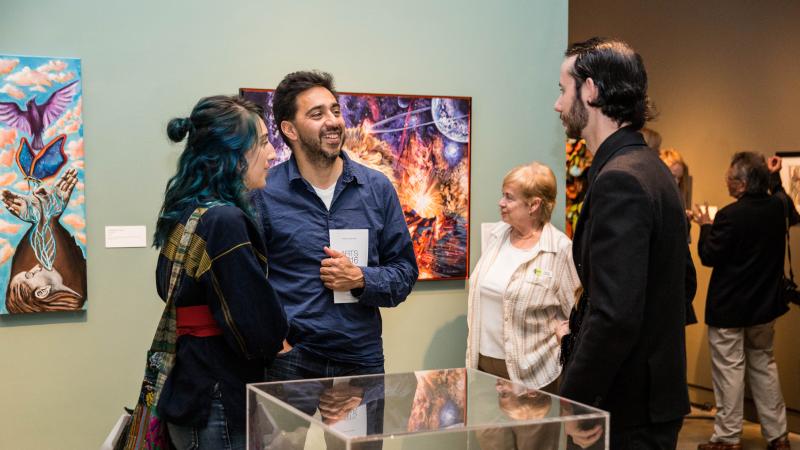 A small group of people talk in an art gallery with sculpture and paintings around them.