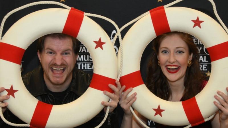 Two actors smile and hold up red and white life buoys