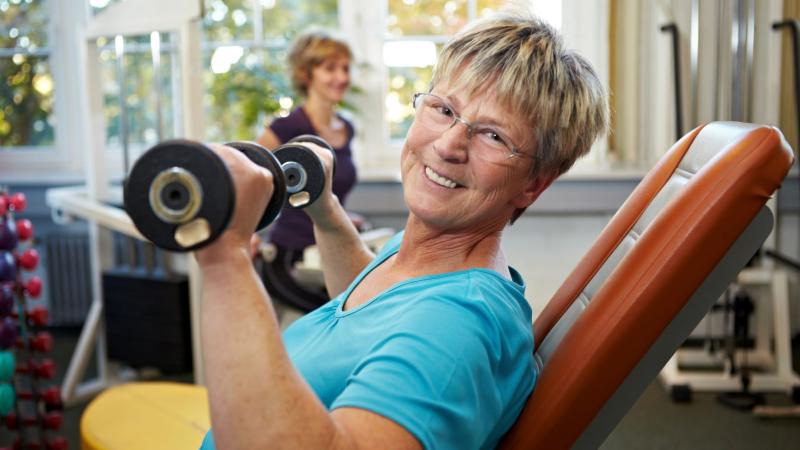 An elderly woman lifting weights at the gym.