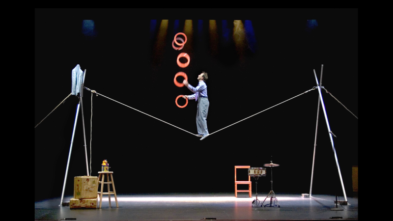 Jamie Atkins juggles red rings while standing on a tight rope