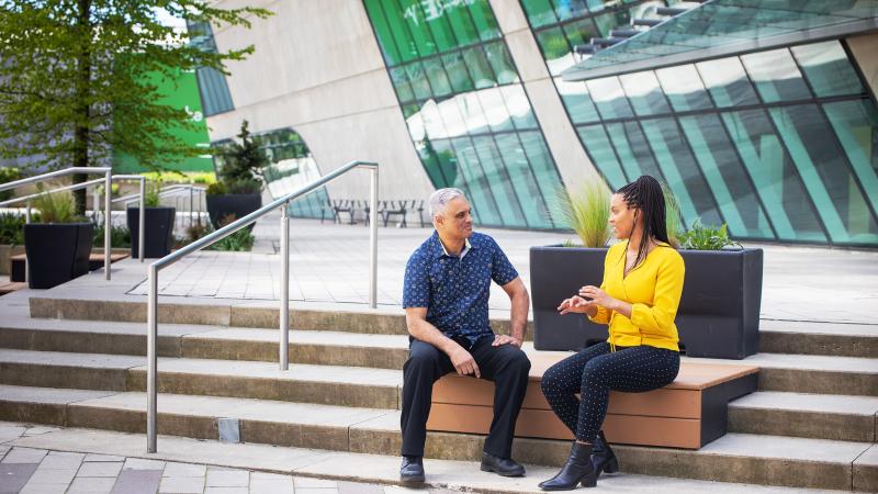 A man and a woman sitting on a bench in front of a library