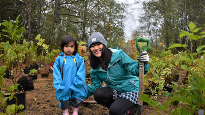 A mother crouching next to her daughter at a tree planting event.