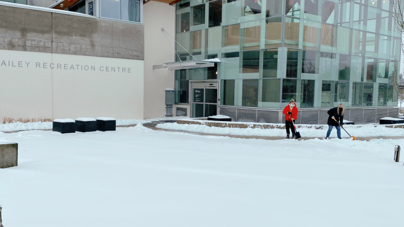 two people shoveling snow in front of chuck bailey recreation centre