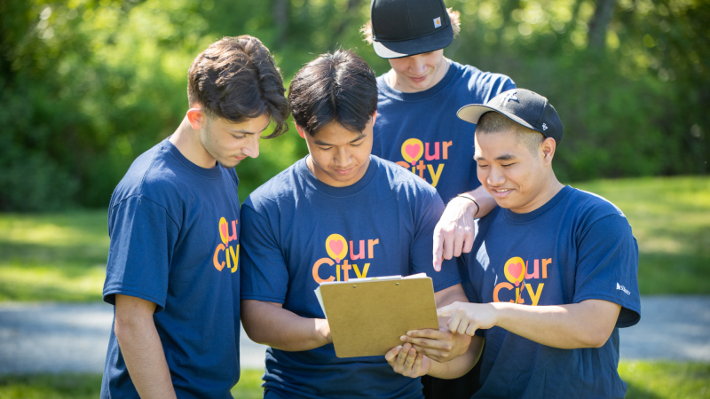 four youth hold a clipboard in a park