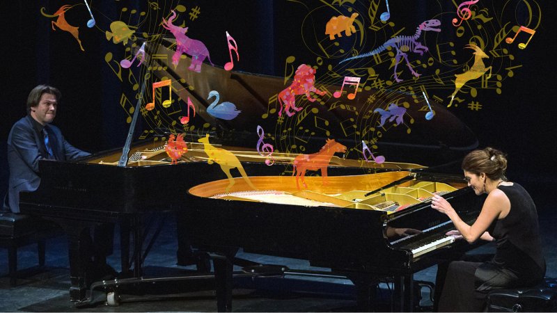 The Bergmann Duo both play a grand piano as a carnival of colourful animals swirl over their heads.