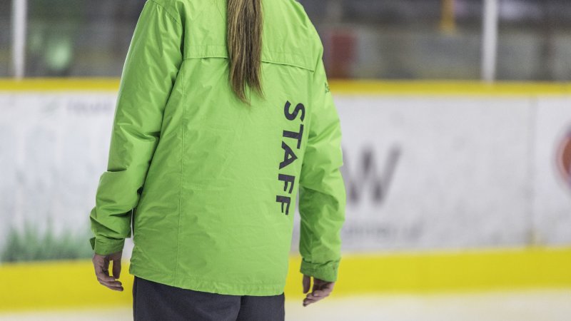The back of an arenas staff wearing a green jacket.