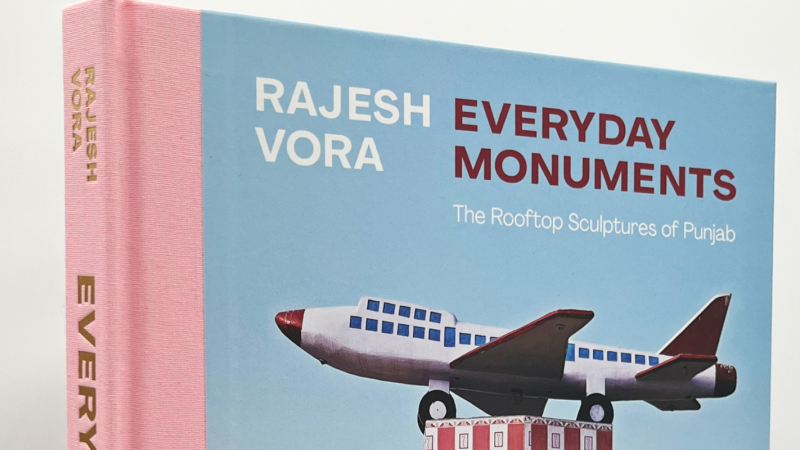 Book cover of Rajesh Vora, Everyday Monuments. The book has a bubblegum pink spine and an image of an airplane against a blue sky.