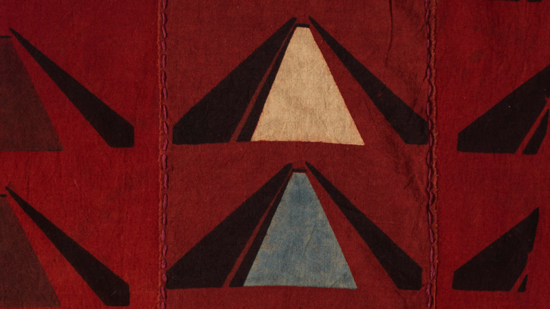 Close up of a red cotton fabric with three triangular shapes repeating in rows of two.