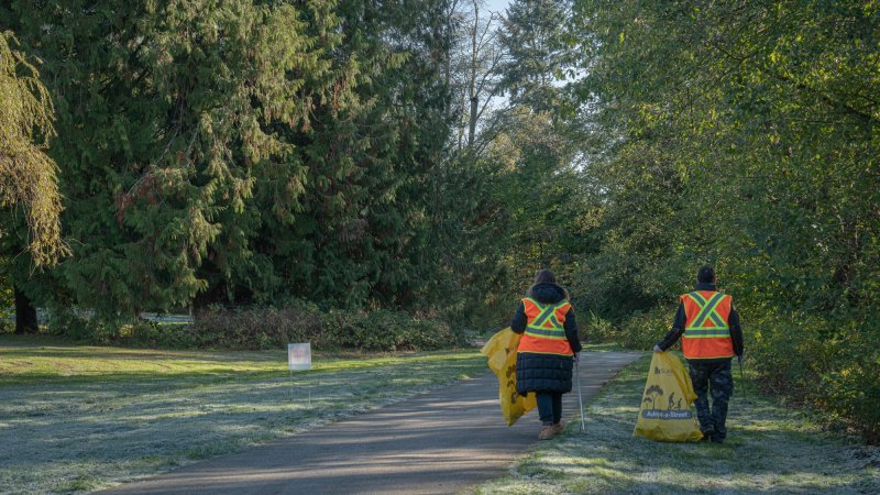 two volunteers in visi vests collect garbage in a park