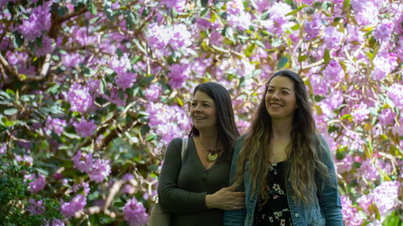 mother and daughter smiling with purple rhododendrons in the background