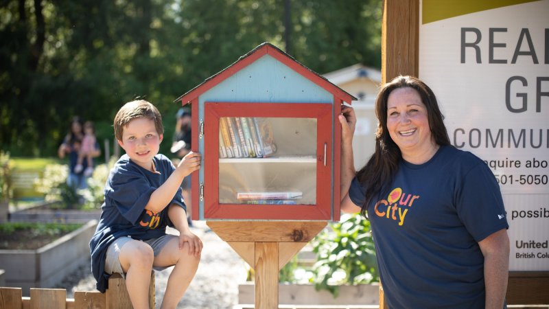 a woman and child pose beside a mini library box